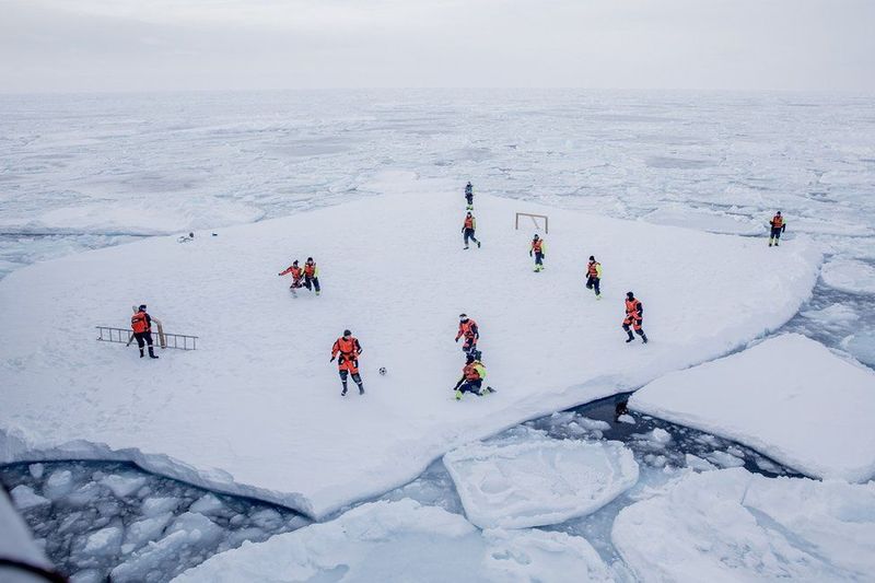 Экипаж норвежского патрульного судна KV Svalbard играет в футбол на льдине в море вокруг Гренландии в марте. Два вооруженных охранника высматривают белых медведей поблизости. Фото: MARIUS VAGENES VILLANGER / AFP